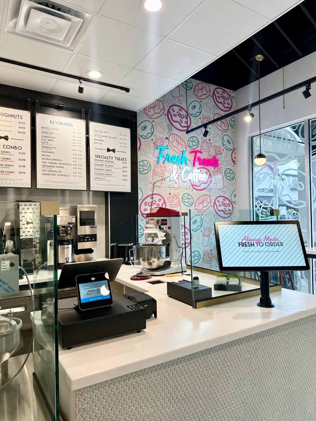 Inside a Dapper Doughnut shop — pinstripe wallpaper, neon Fresh Treats & Coffee sign, and digital menu boards